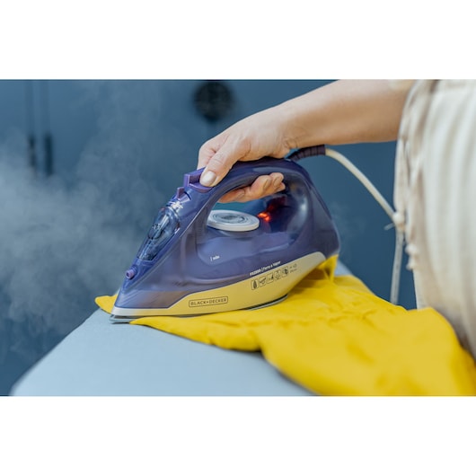 Photo of BLACK+DECKER FX2550 steam iron in use on yellow fabric, handheld, visible steam, shown from side angle.