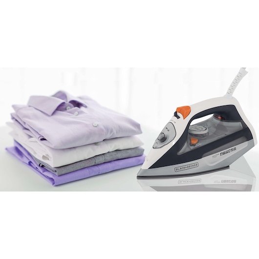 A BLACK+DECKER steam iron is placed on a reflective surface next to a neatly folded stack of shirts in various pastel and neutral colors.