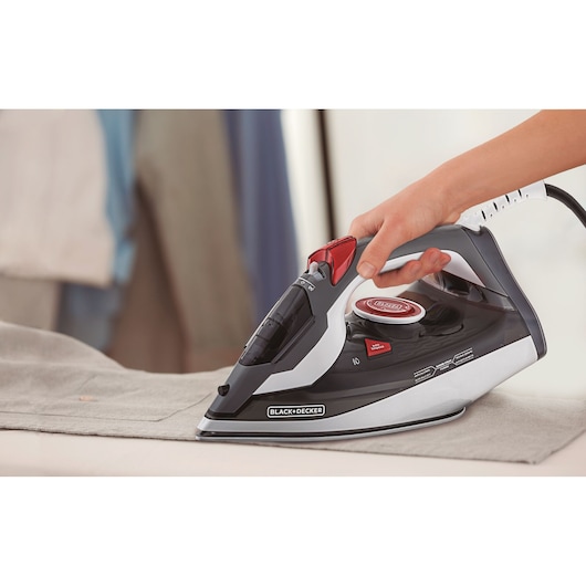 Photo of BLACK+DECKER FX900 steam iron in black and red, handheld, ironing a gray shirt.