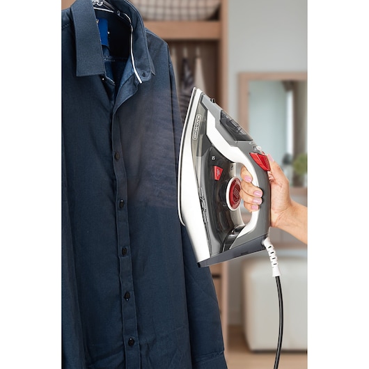 Photo of BLACKDECKER FX900 steam iron being used to iron a navy blue shirt in a home setting.