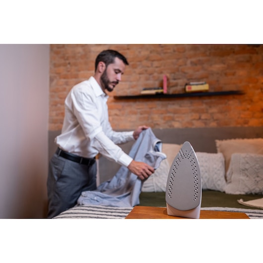 BLACKDECKER FXVG1 steam iron on table with person holding shirt in bedroom setting.