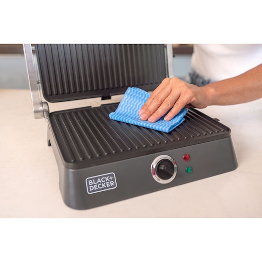 Photo of BLACKDECKER G1400 contact grill being cleaned with a blue cloth, close-up on grill plate.