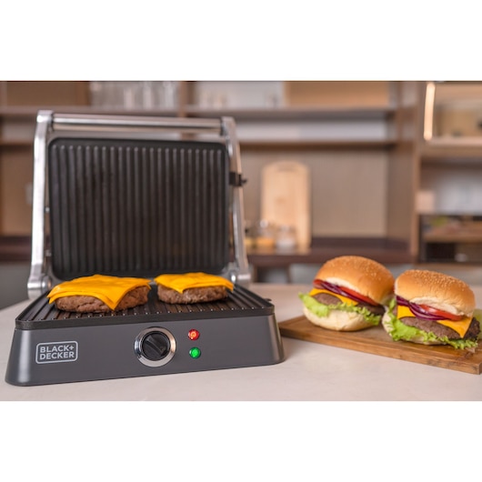 Photo of BLACKDECKER G1400 electric grill cooking cheeseburgers, with two finished burgers on a wooden tray, kitchen background.