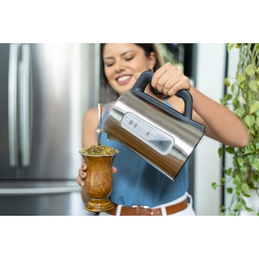 BLACKDECKER KEPG electric kettle pouring hot water into a mate cup with metal straw in a kitchen.