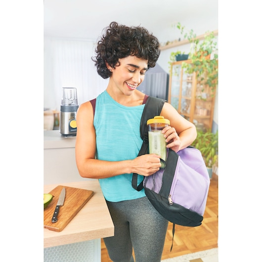 Photo of a person holding a BLACKDECKER LP320 blender cup with yellow lid and a purple gym bag in a kitchen.