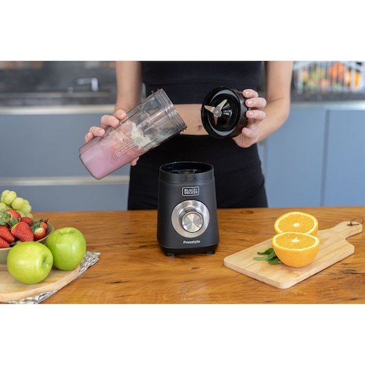 Photo of BLACK+DECKER LP420 blender on a wooden table, person assembling with fruit and orange halves nearby.