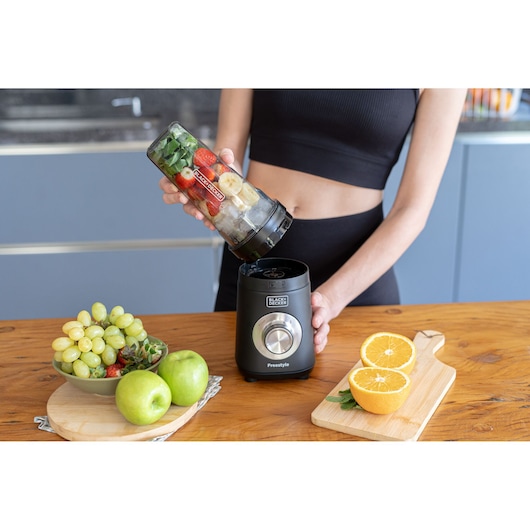 Photo of BLACKDECKER LP420 blender on a kitchen counter, a person adding a filled blending jar, with fruit nearby.