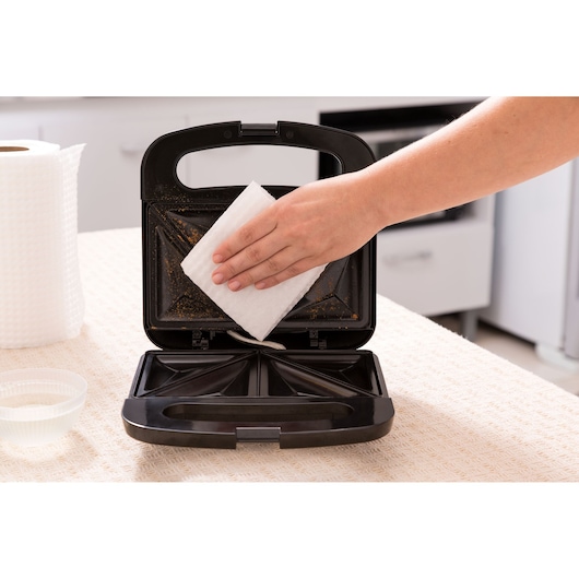 Photo of BLACKDECKER SM800 sandwich maker being cleaned with a white cloth in a kitchen setting.