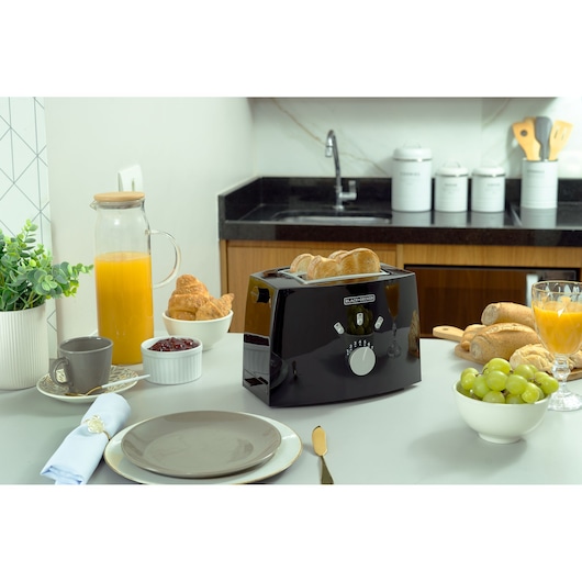 Photo of BLACKDECKER TO810 black toaster on a kitchen table with bread, juice, coffee, grapes, and breakfast items.