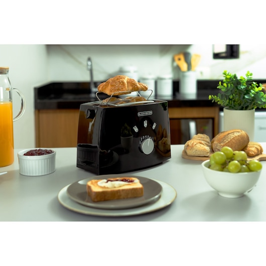 BLACK+DECKER TO810 black toaster with croissant on top, surrounded by breakfast foods on a kitchen counter.