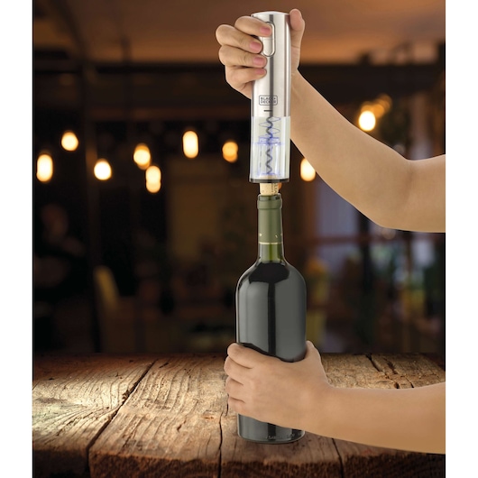 BLACK+DECKER W10 electric wine opener being used to uncork a wine bottle on a wooden table.